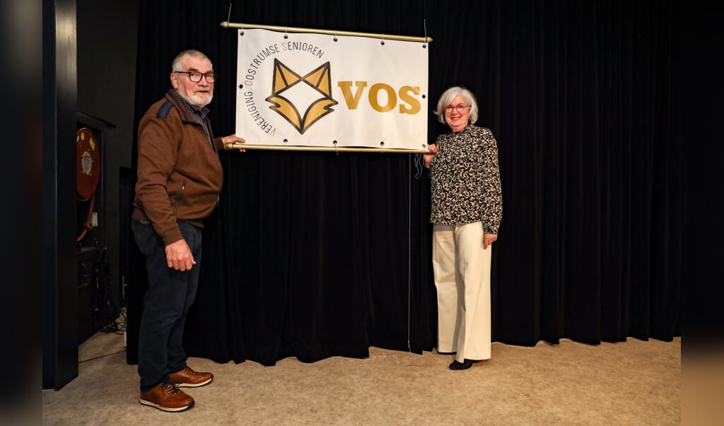 Voorzitter Jan Kreutz en bestuurslid en naambedenker Gerrie Daniels poseren bij het nieuwe logo van VOS. 