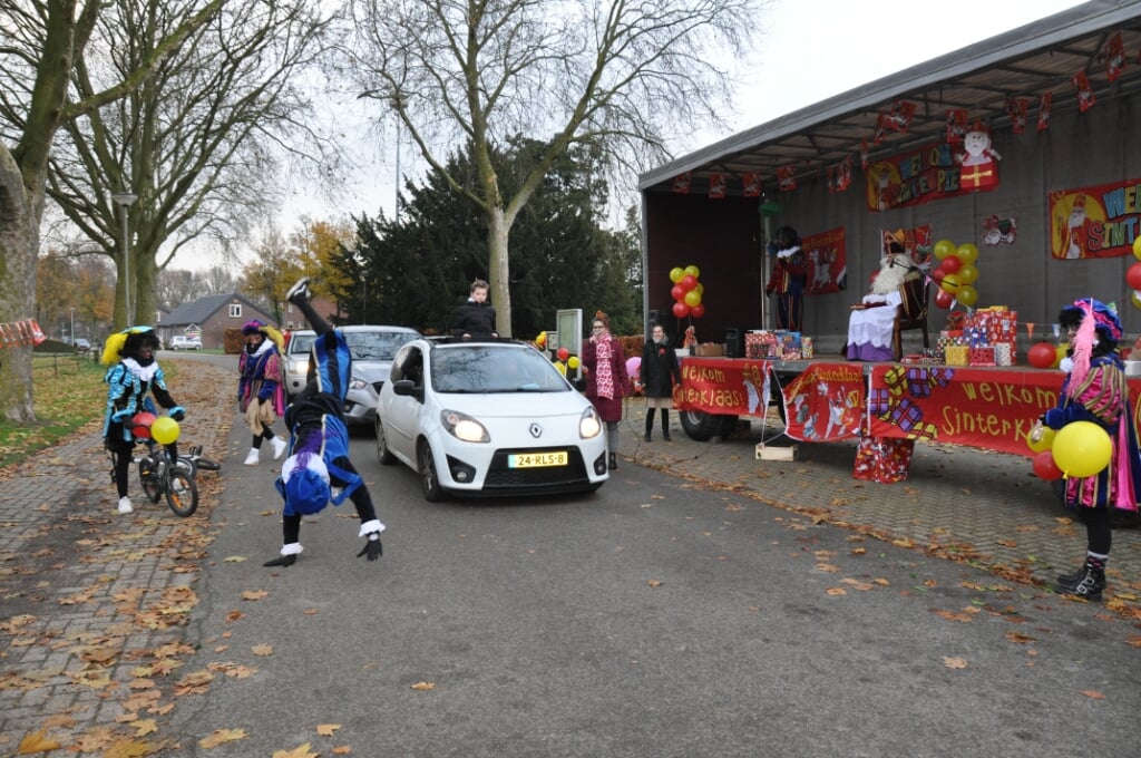 De kinderen zwaaien vanuit de auto naar Sinterklaas die vanuit een open trailer tevreden toekijkt.