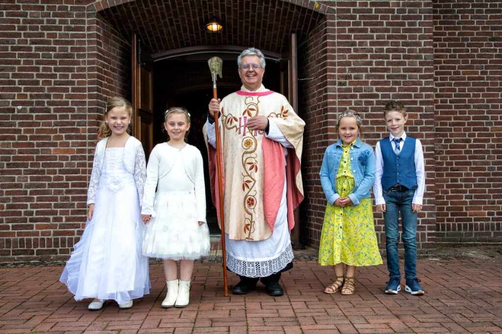 Pastoor Clemens met vier lachende communicantjes voor de kerk
