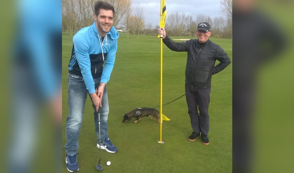 Dennis Zwarts van GO Sport & Cultuur put op hole 18 op golfbaanCatharinenburg. Golfleraar Leo van Bennekom bewaakt de vlag.