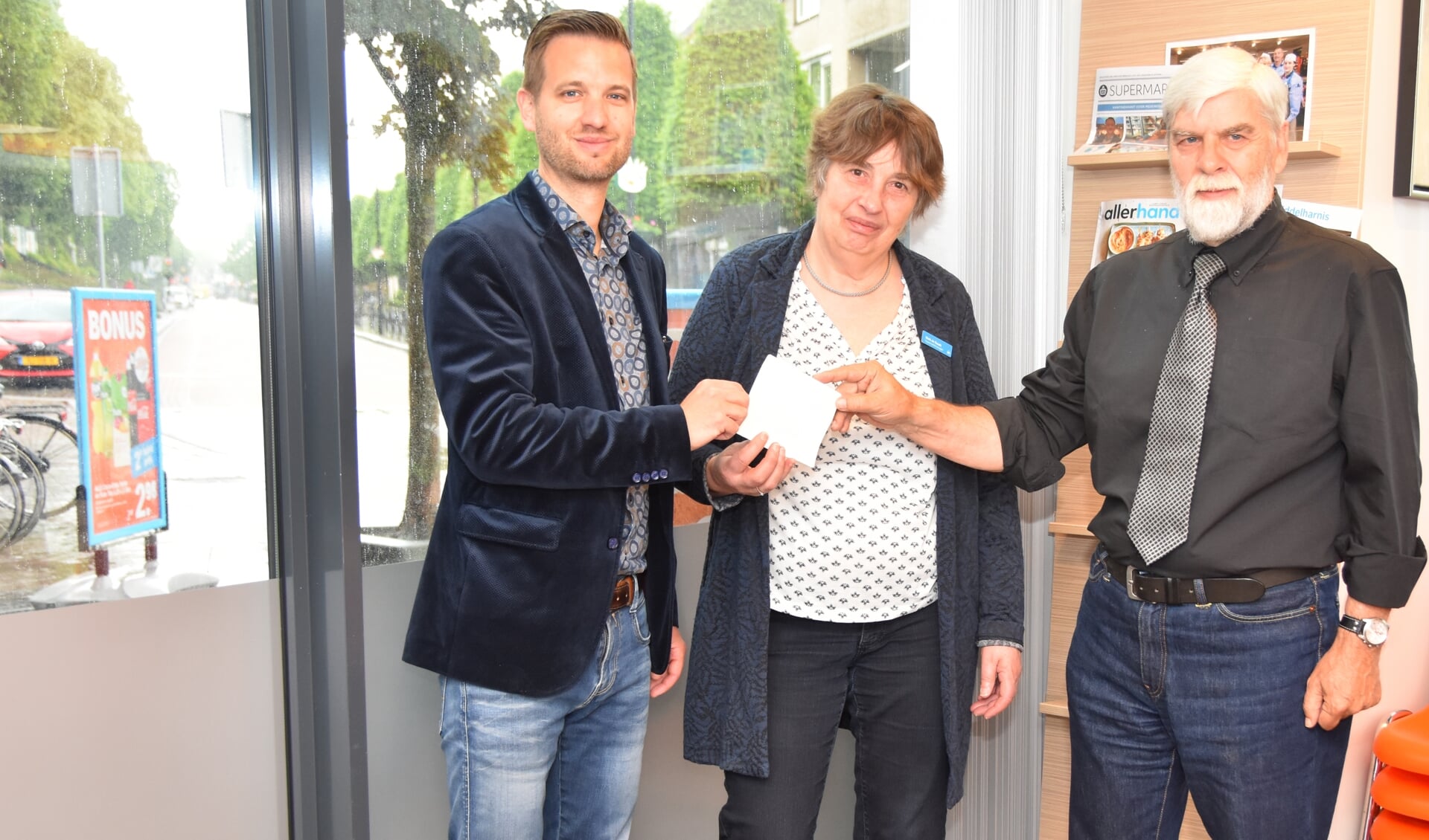 Wim Eijbers, voorzitter van de afdeling Alzheimer Nederland overhandigt de stickers aan de beide filiaalhouers, Meik de Raadt en Jasper Pieterse. 