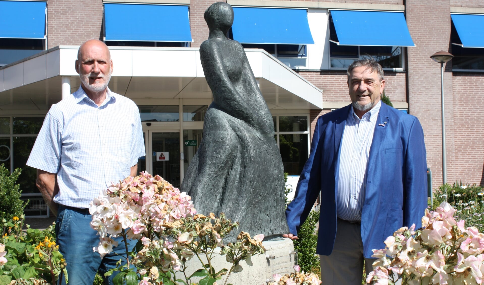Henk Zwanenburg (links) en Jan Leenders bij het beeld van Paulina van Weel, recht voor de hoofdingang van het ziekenhuis in Dirksland (Foto: Kees van Rixoort).