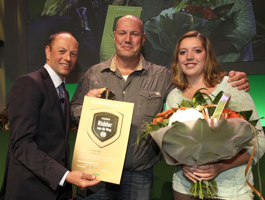 Peter van Sluijs (midden) uit Stellendam ontving de oorkonde die hoort bij de onderscheiding Gouden Ridder van de weg. Rechts zijn dochter Maureen.
