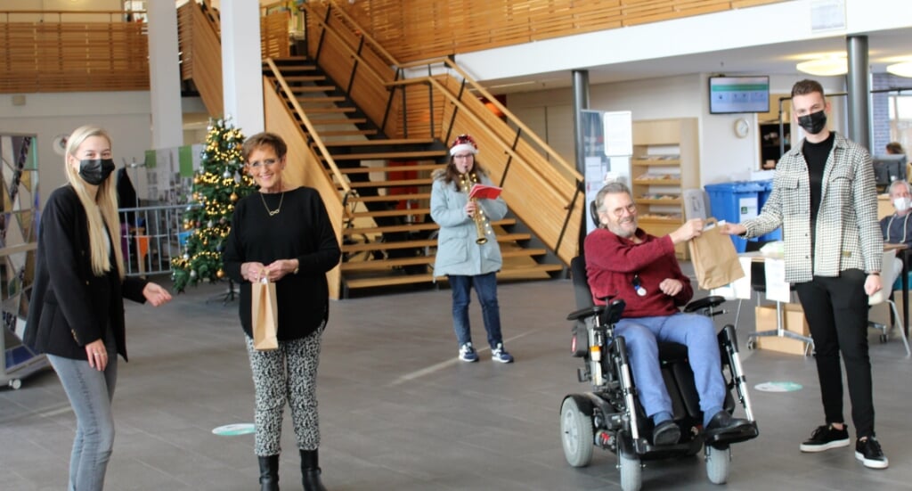 Nina Plooij (links) en Rick van der Welle (rechts) overhandigen de tasjes aan Yvonne van Voorst en Leen Bolier, bewoners van Nieuw Rijsenburgh. Sanne Smeets (midden) speelt kerstliedjes (Foto: Mirjam Terhoeve). 