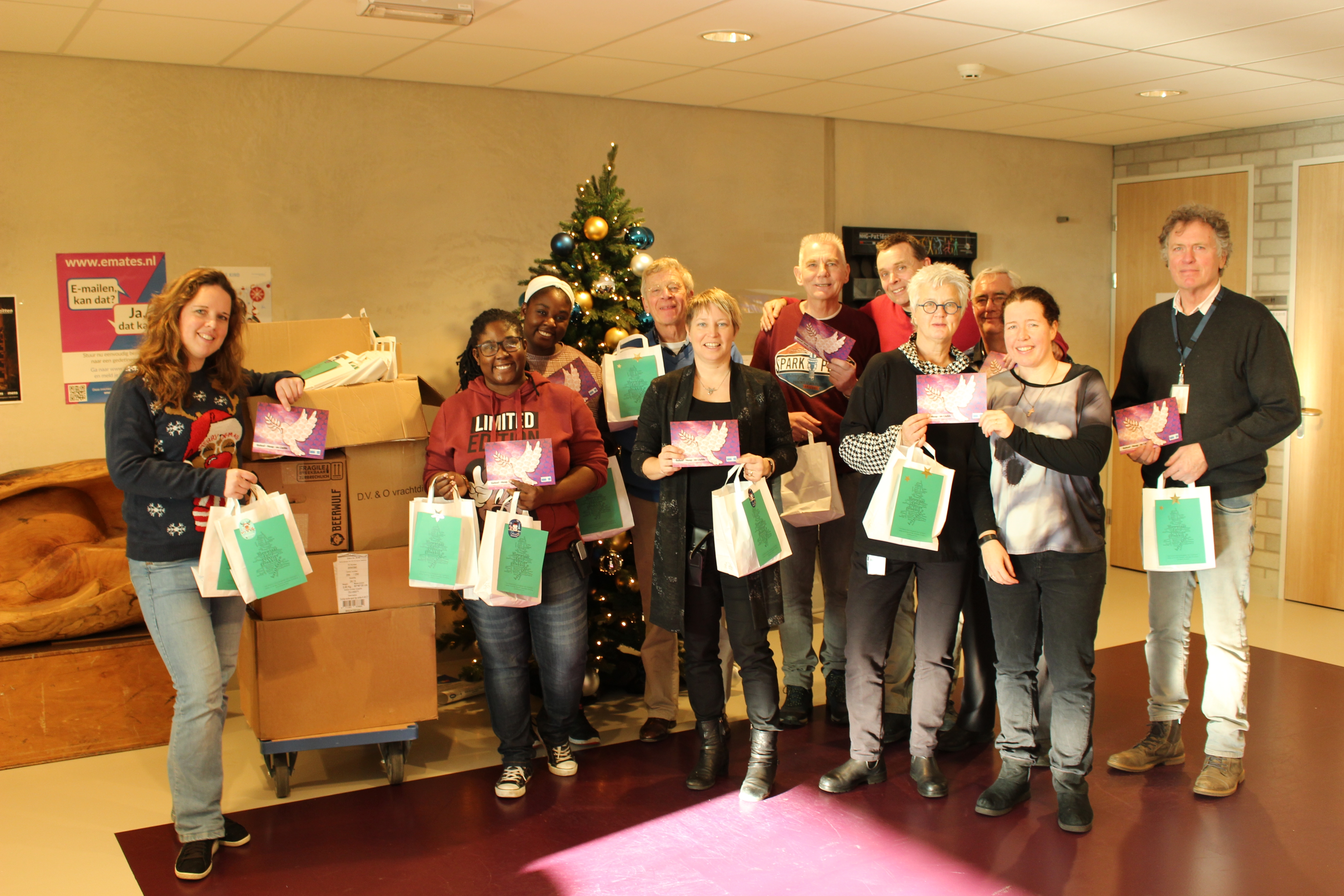 Vrijwilligers DSG De Sluis en medewerkers Geestelijke Verzorging JCZ Zaanstad delen attenties uit. Links de kar met de 850 pakketjes.