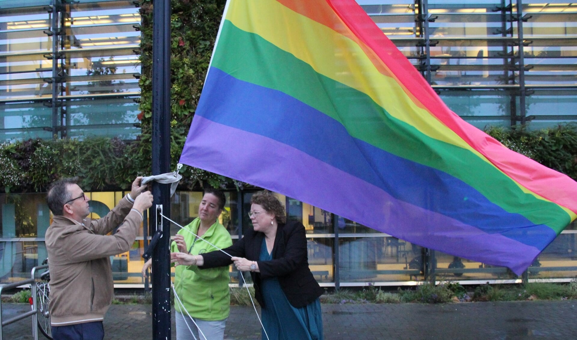 Wethouder Annette Valent (r) en Suleika van Holland van MET (m) hijsen de regenboogvlag op het Stadsplein.