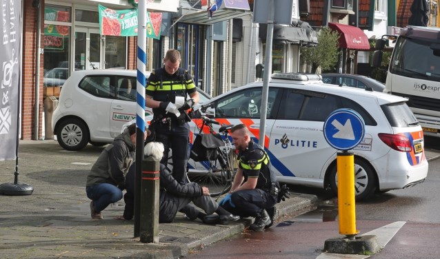 Agenten en een omstander verlenen de vrouw na de valpartij eerste hulp.