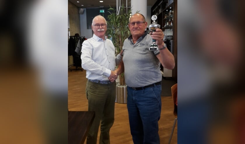 De voorzitter (links) heeft Willem zojuist de beker overhandigd.