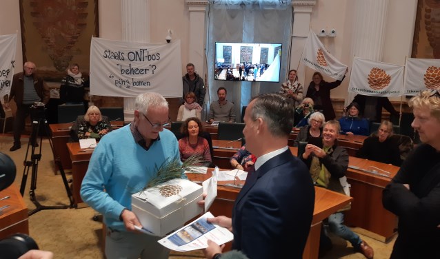 Voorzitter Jan Engelbregt biedt het burgerinitiatief aan met 8.570 handtekeningen, verlucht met een dennentak.
