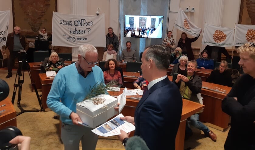 Voorzitter Jan Engelbregt biedt het burgerinitiatief aan met 8.570 handtekeningen, verlucht met een dennentak.