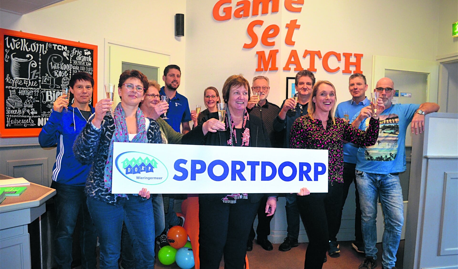 Wethouder Mary van Gent toont een Sportdorp-bord temidden van de partners van Sportdorp Wieringermeer.