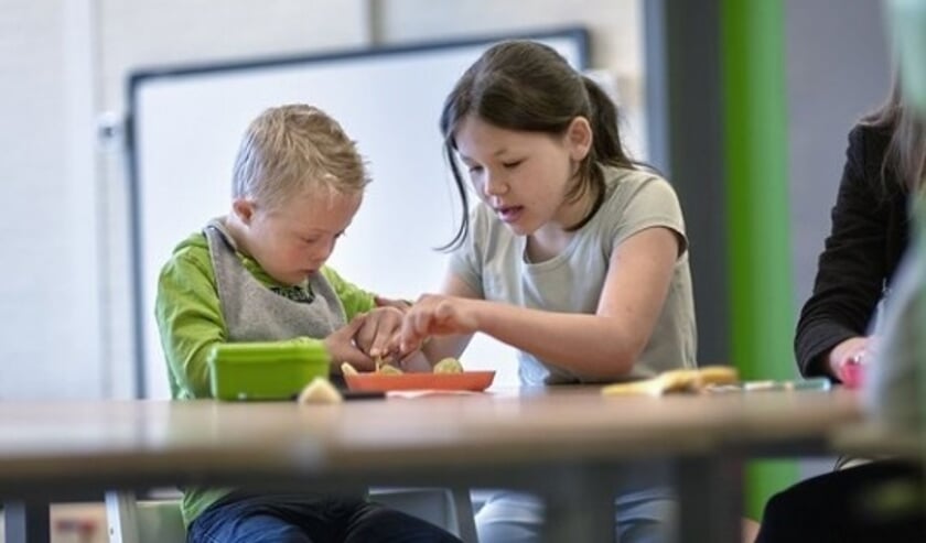 Een beperkte jongen krijgt een handje hulp van een klasgenootje bij het klaarmaken van fruit.
