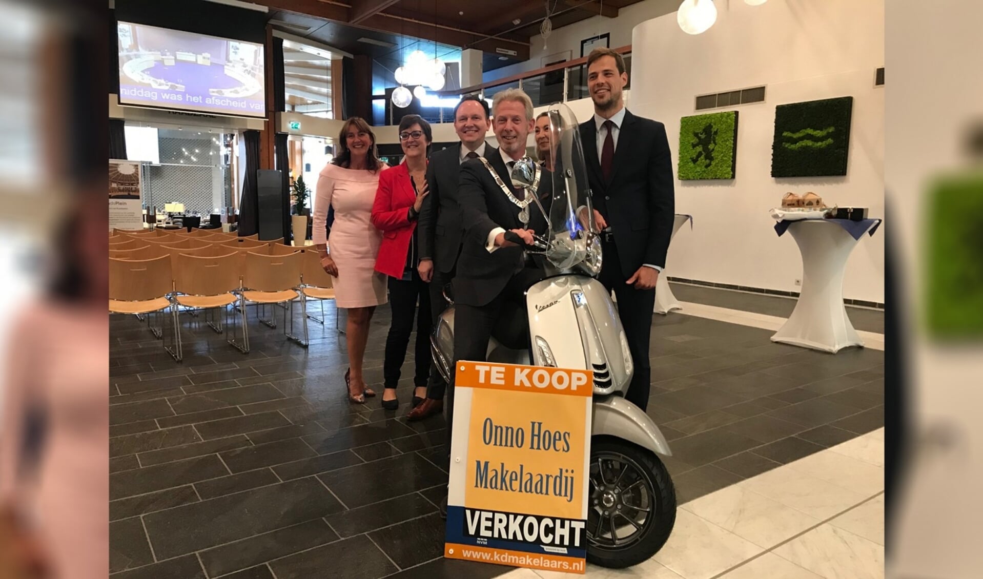 Waarnemend burgemeester Onno Hoes poseert in de raadszaal op de zojuist overhandigde makelaarsscooter. 