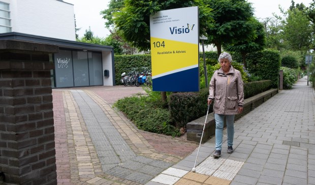 Blinde vrouw loopt met taststok over geleidelijn.