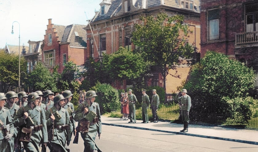 Soldaten marcheren in 1942 over de Alkmaarse Kennemerstraatweg op deze ingekleurde foto.