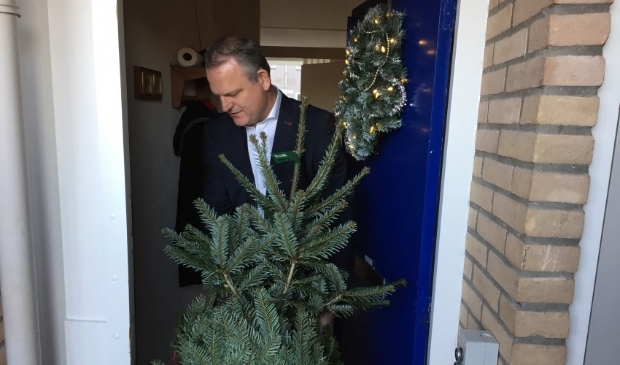 <p>Wethouder Gerard Slegers (openbare Ruimte) brengt een kerstboom langs bij een van de bewoners van Pennemes </p>