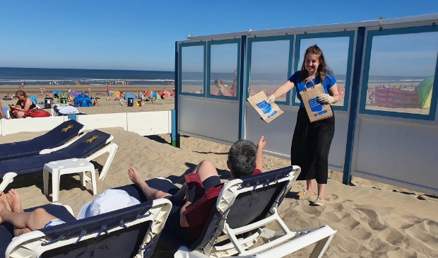 <p>Vrijwilliger van Stichting De Noordzee deelt zakjes uit aan badgasten.</p>