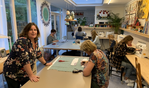 <p>Coupeuse Anne-Marie Smulders (l) in haar naaischool met de dames van de donderdagavond.</p>