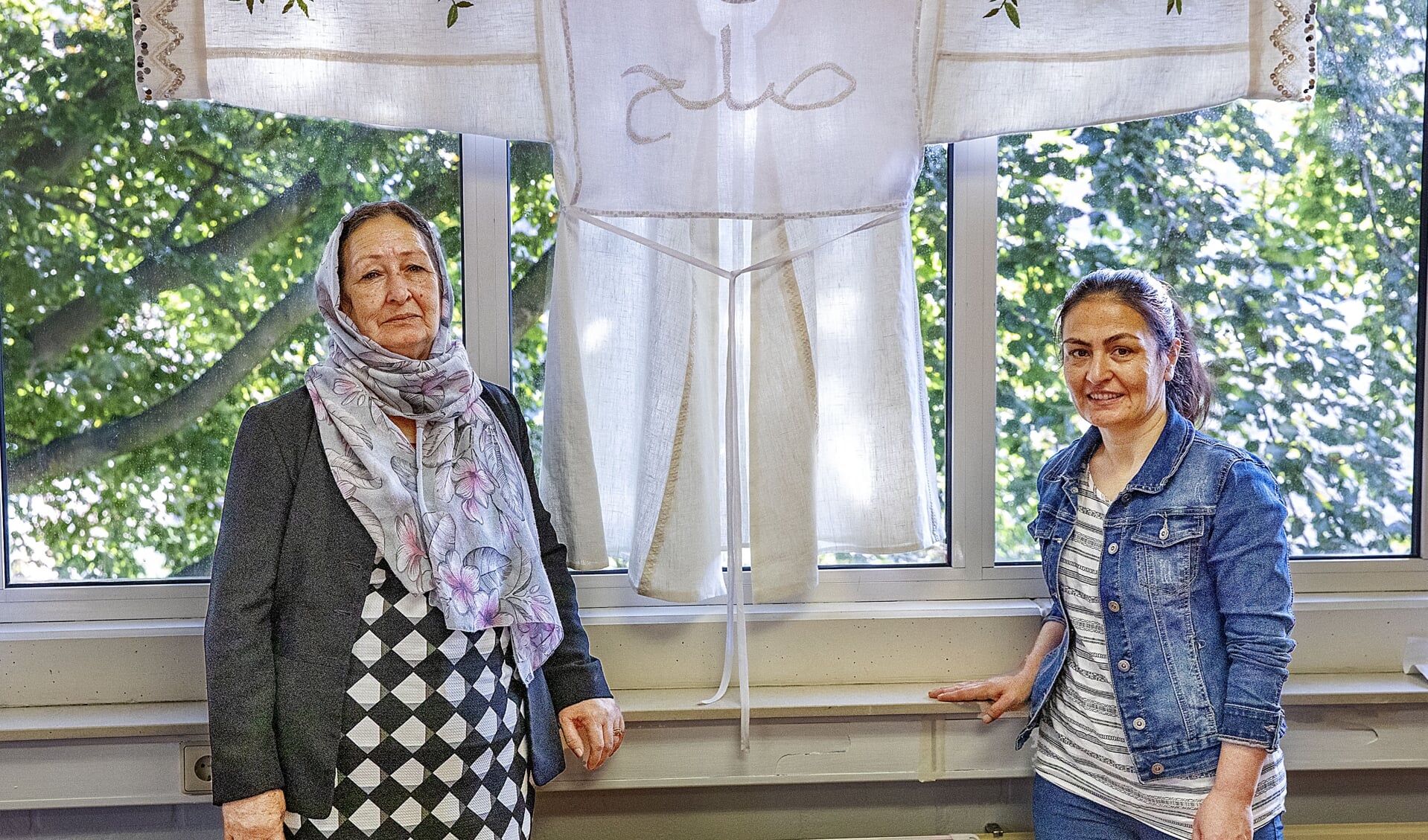 Nasima en Zakya bij de traditionele Afghaanse jas die zij in het kader van de Vredesweek maakten. Op de jas is in het Dari, een van de officiële talen in Afghanistan, het woord voor 'vrede' geborduurd.