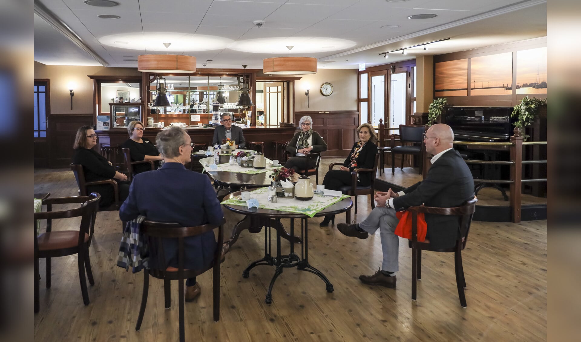 In het Grand Café van woonzorglocatie De Hoge Hop in Hoorn, waar voor de coronamaatregelen activiteiten en samenkomsten voor bewoners plaatsvonden, bespreken de deelnemers aan het werkbezoek de situatie in de zorg. 