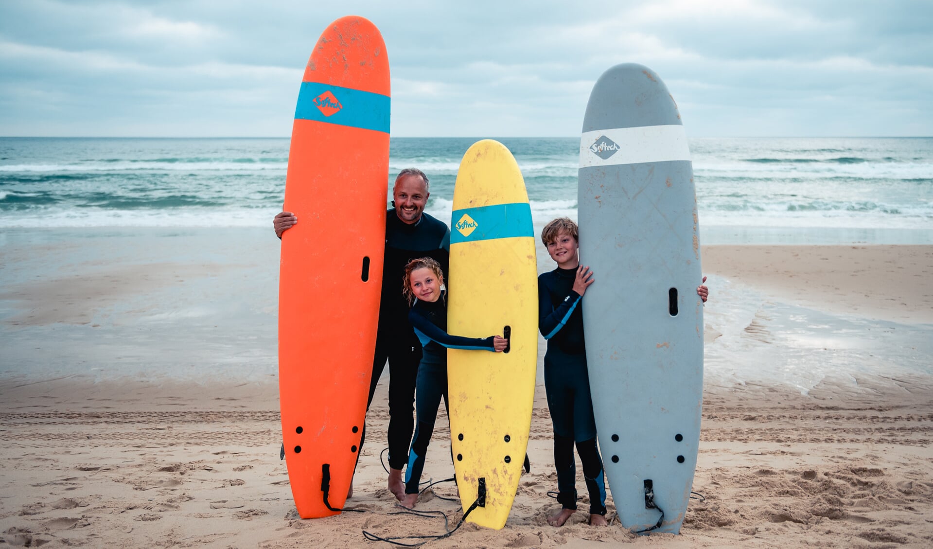 Vader met zijn kinderen surfen op het strand van Bloemendaal.