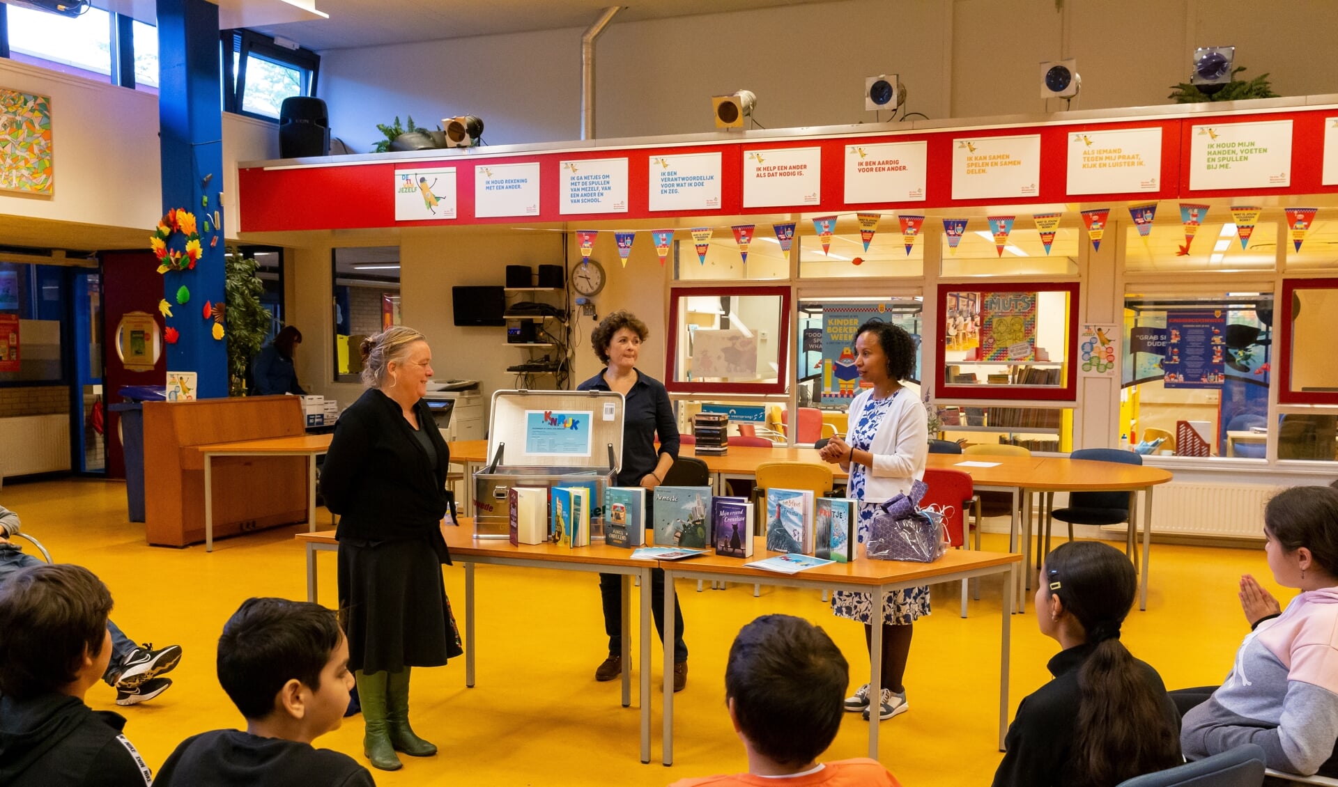 Stadsdeelbestuurder Esther Lagendijk, Marianne Mondeel (OBA) en Rochelle Heerema presenteren de leskist aan leerlingen van basisschool De Vier Windstreken.