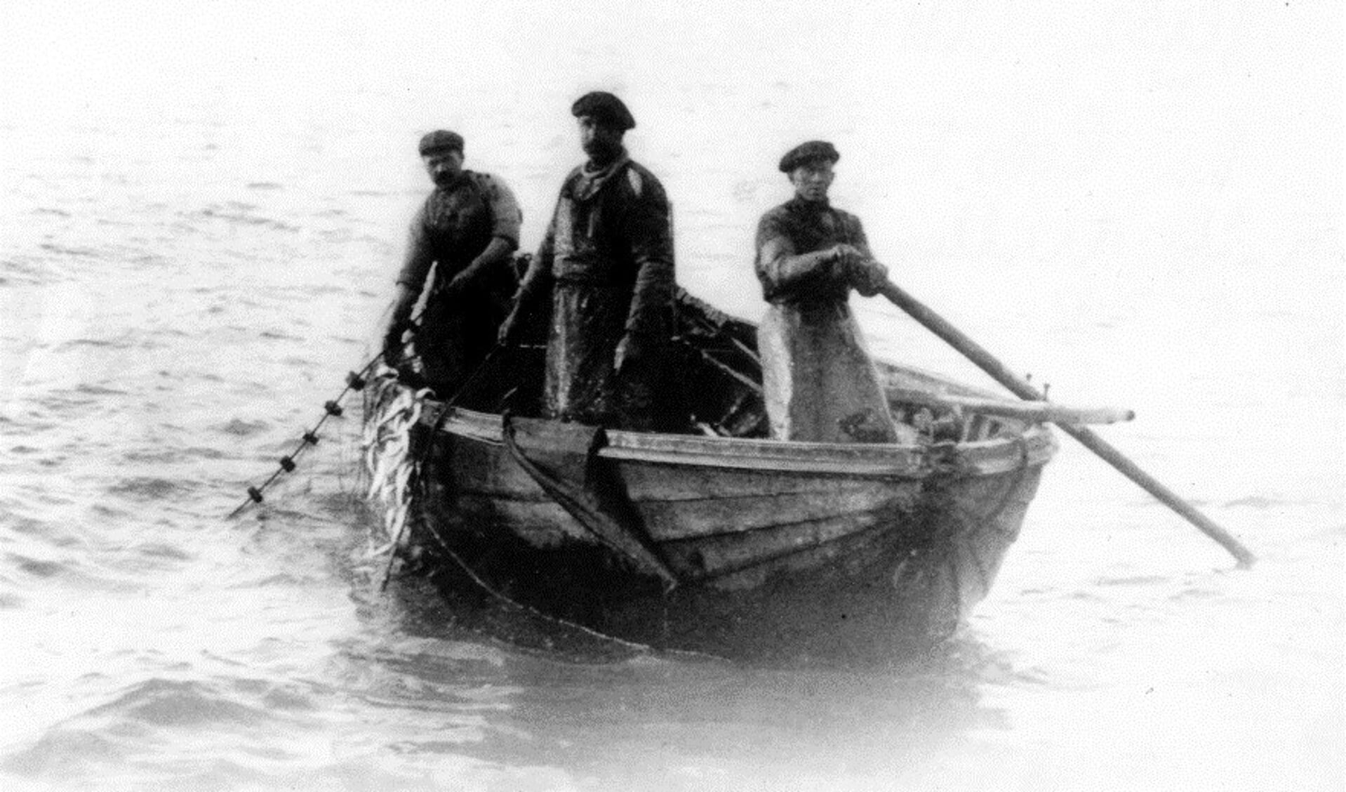 Foto uit 1932 van de vissers Cees Fijma, Willem Visser en K. de Graaf tijdens de ansjovisvisserij. De staande netten met de gevangen ansjovis worden binnengehaald. Ansjovisvlet EH 97.