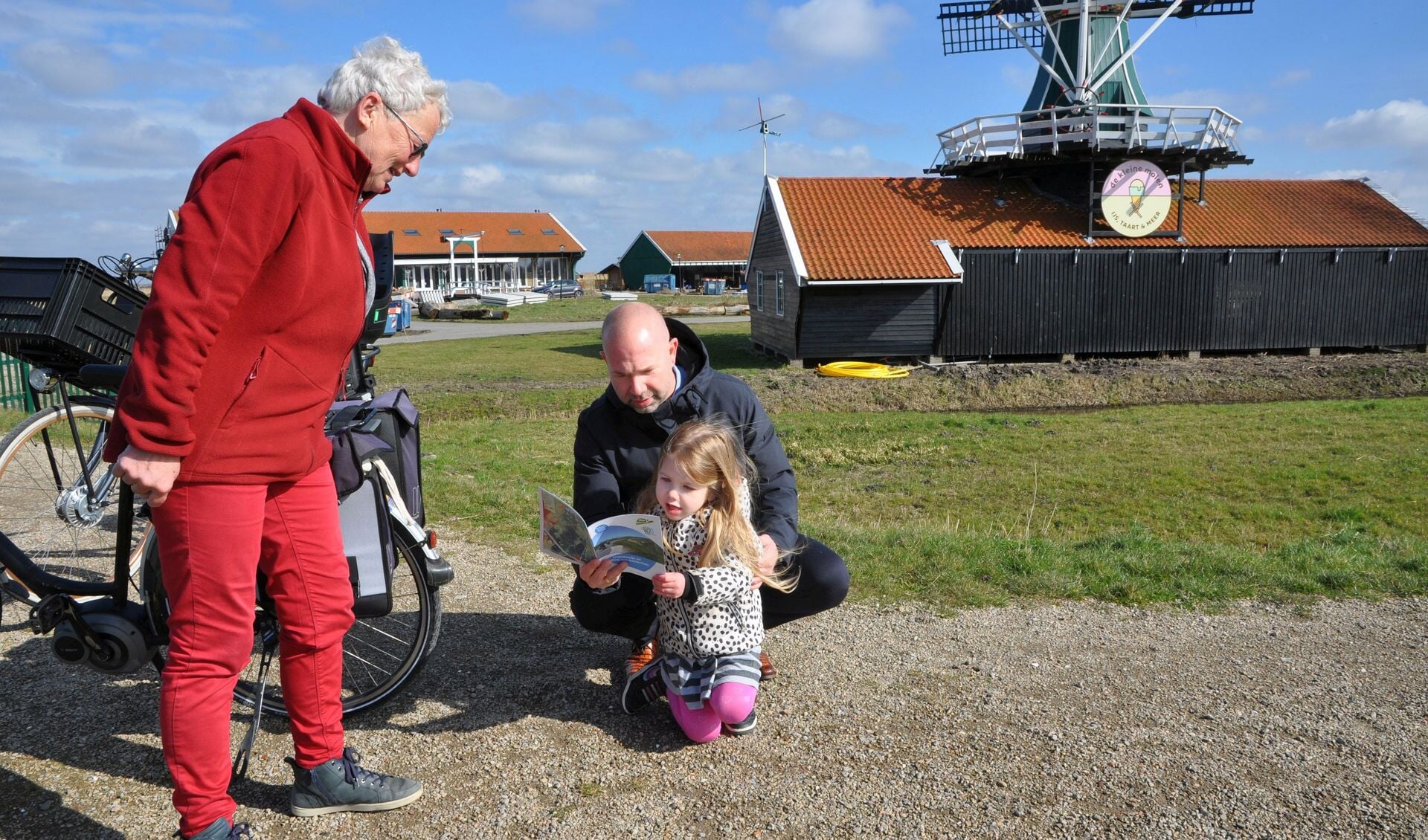 Burgemeester Sebastiaan Nieuwland van Uitgeest bekijkt met zijn dochter Julia het nieuwe routeboekje Crommenije en De Stelling. Samenstelster Lia Vriend van de Stichting Oer-IJ heeft het hem net het eerste exemplaar overhandigd. 