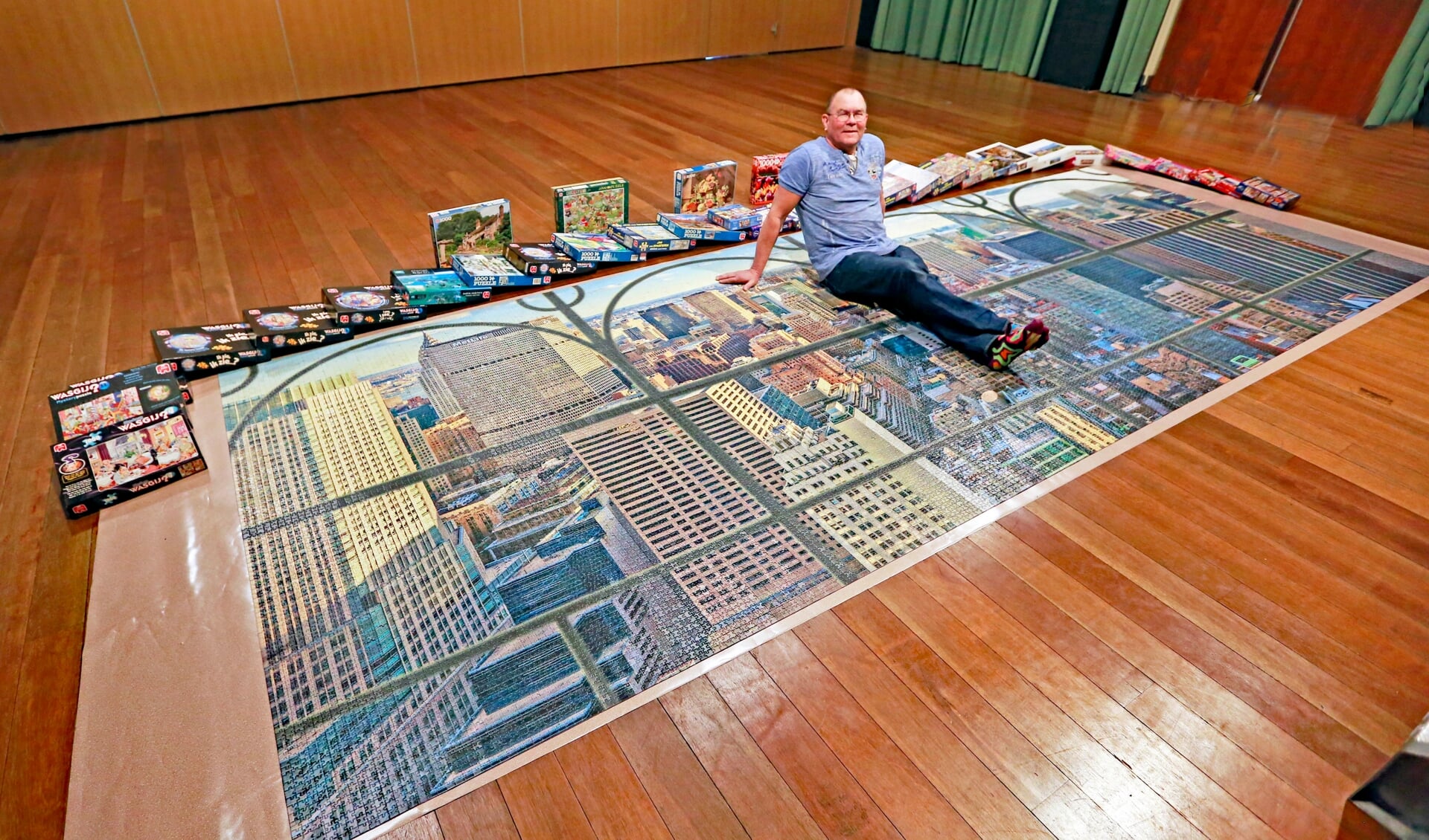 Cees poseert op zijn puzzel van 24.000 stukjes. De puzzels eromheen zijn te leen.