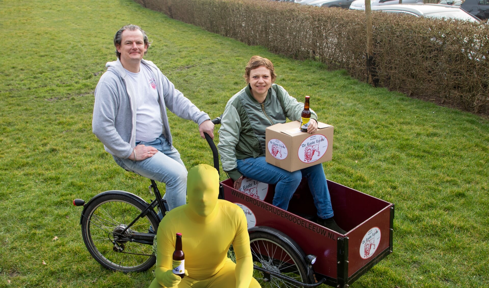 Dyon Huiberts overhandigt aan Esther Vinke het gebrouwen Intermezzo Bier. Op de voorgrond het vrolijke gele mannetje.