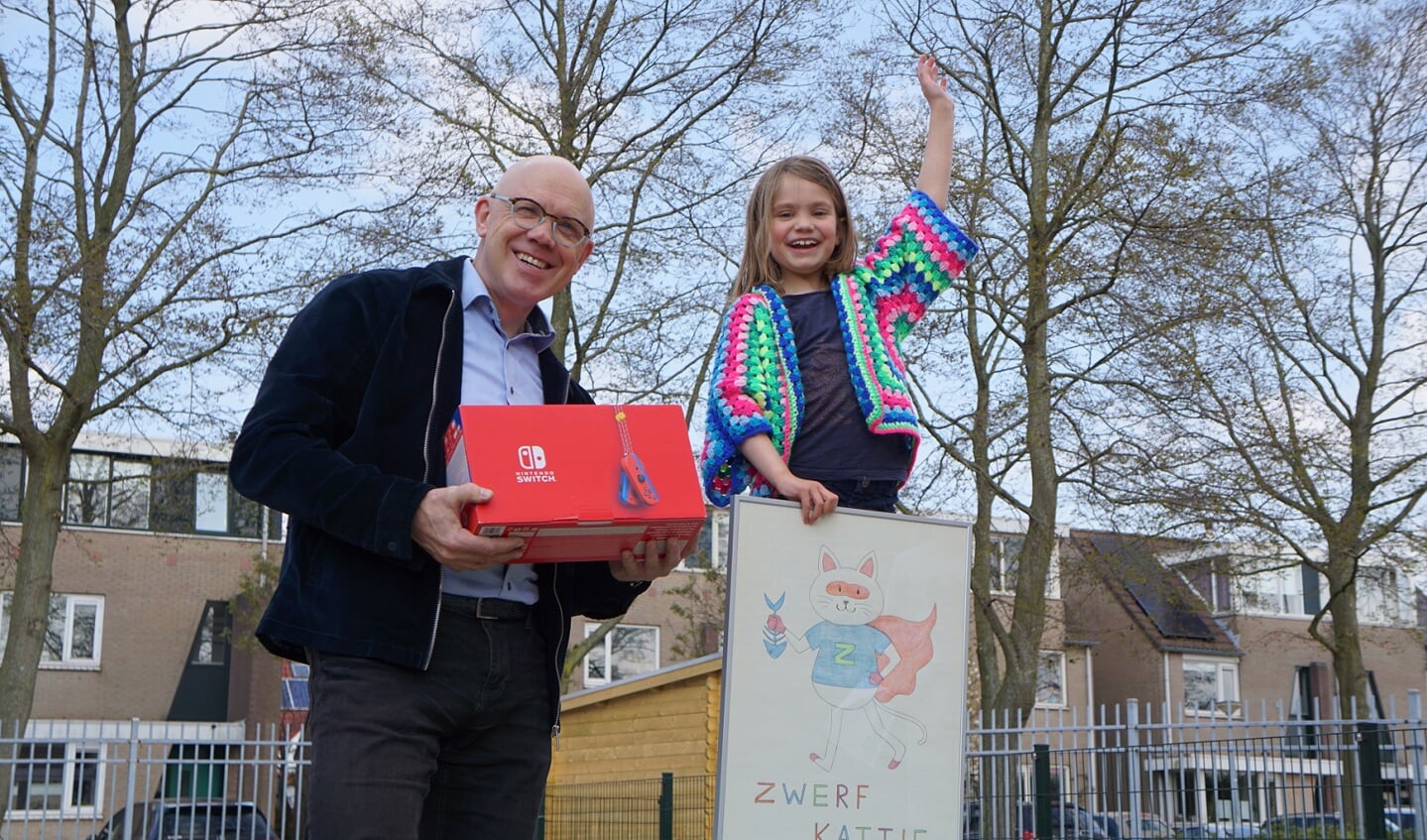 Wethouder Harold Halewijn reikt aan winnaar Mara een Nintendo Switch uit op het schoolplein als blijk van waardering voor haar winnende inzending. 