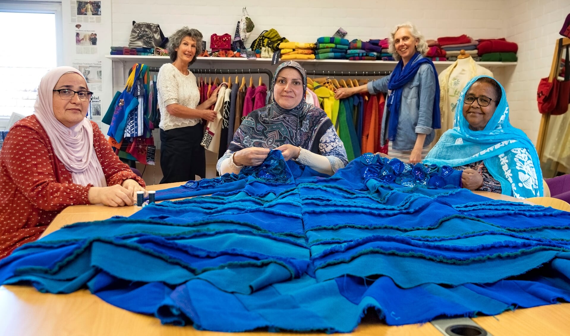 Tara, Israa en Akberet (v.l.n.r.) werken aan de jas die in het kader van Wereldvluchtelingendag tentoongesteld wordt. Op de achtergrond Marilou Evelo (l) en Gerda Schoenmaker.