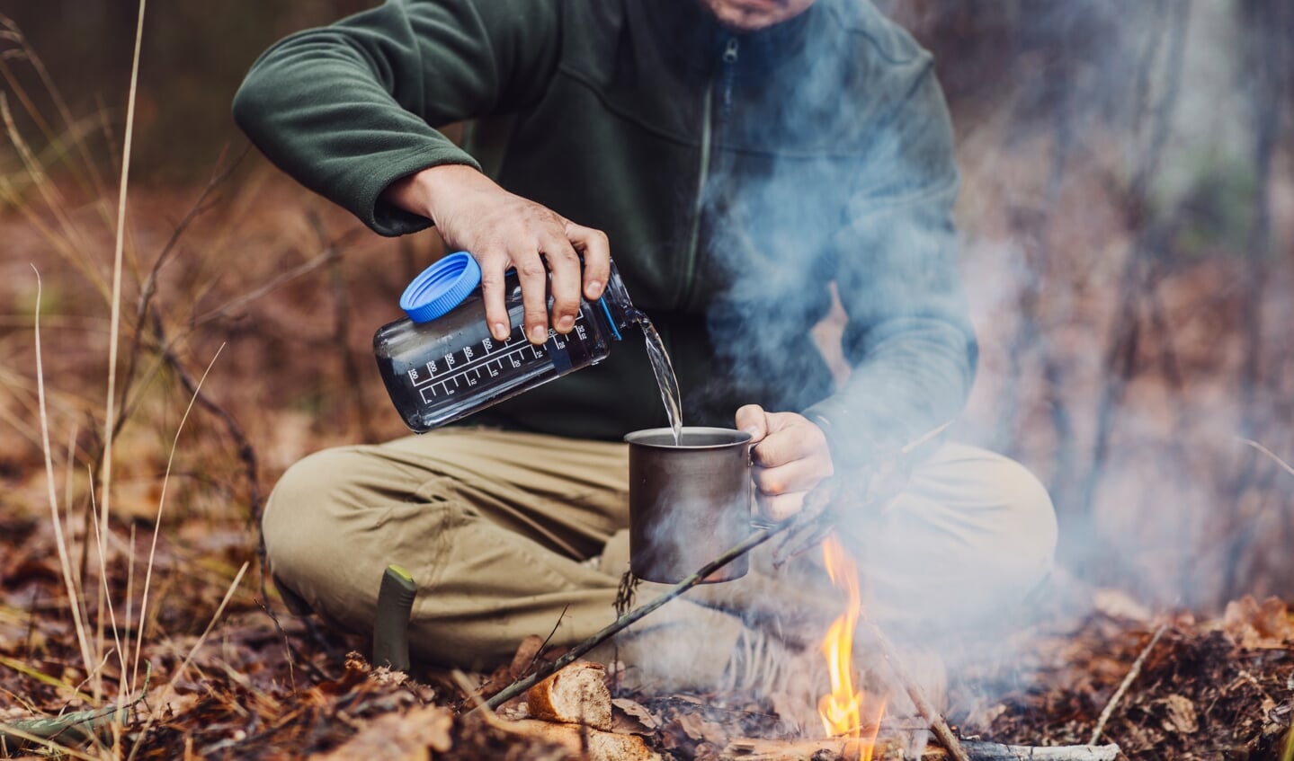 hunter pours water from a bottle into a metal mug. bushcraft, adventure, travel, tourism and camping concept.