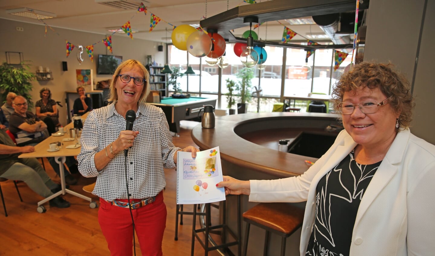 Carolien Langedijk (links) reikt het jubileumboekje uit aan wethouder Annette Groot.