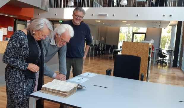 <p>Paul Rietmeijer en Ytje Visser bekijken samen met Peter Swart (r) een zeventiende-eeuws belastingregister. </p>