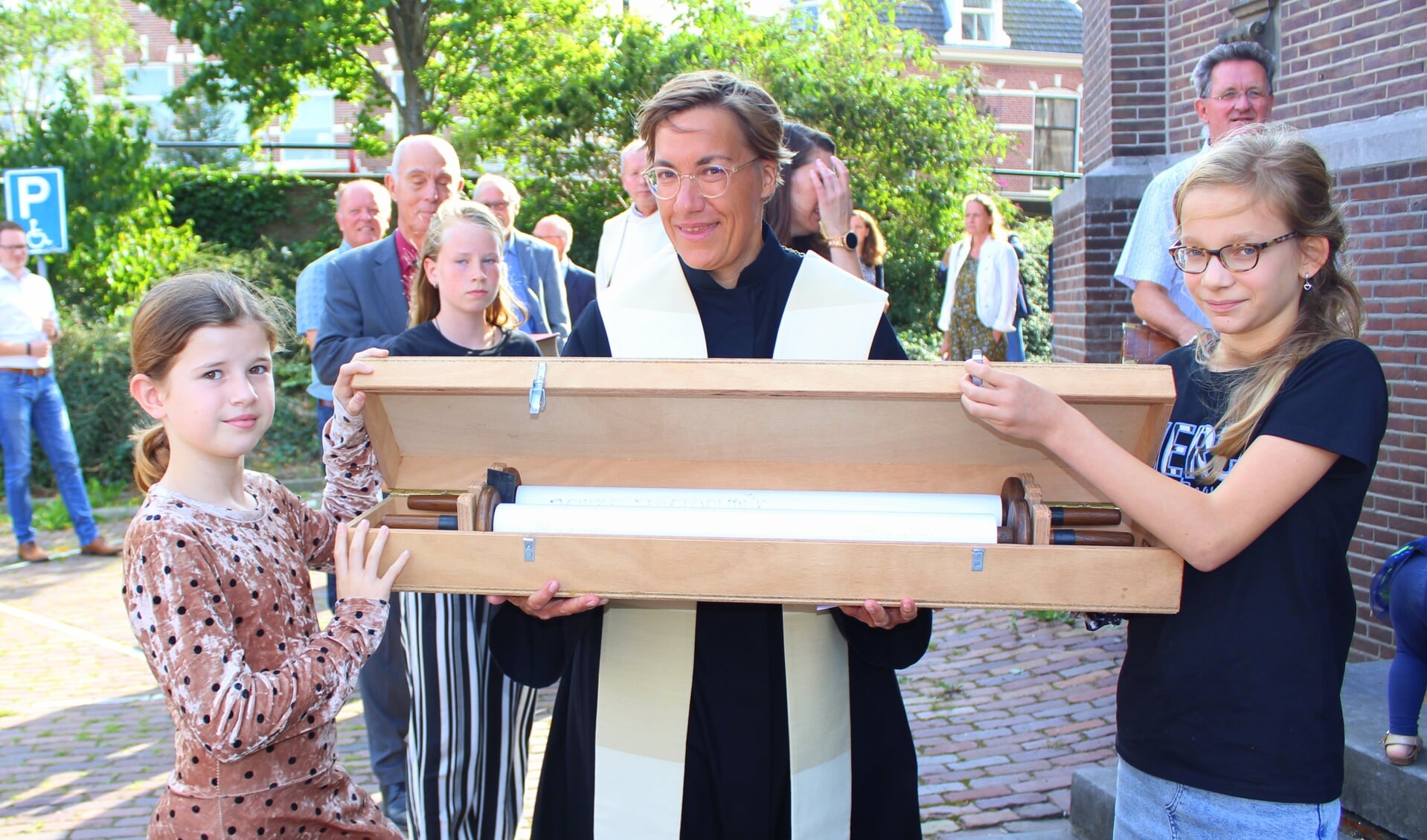 Predikante Anne-Marie van Briemen begeleidt Linn (li) en Menthe bij het overdragen van de dooprollen, van de Zijdekerk naar de Dorpskerk.