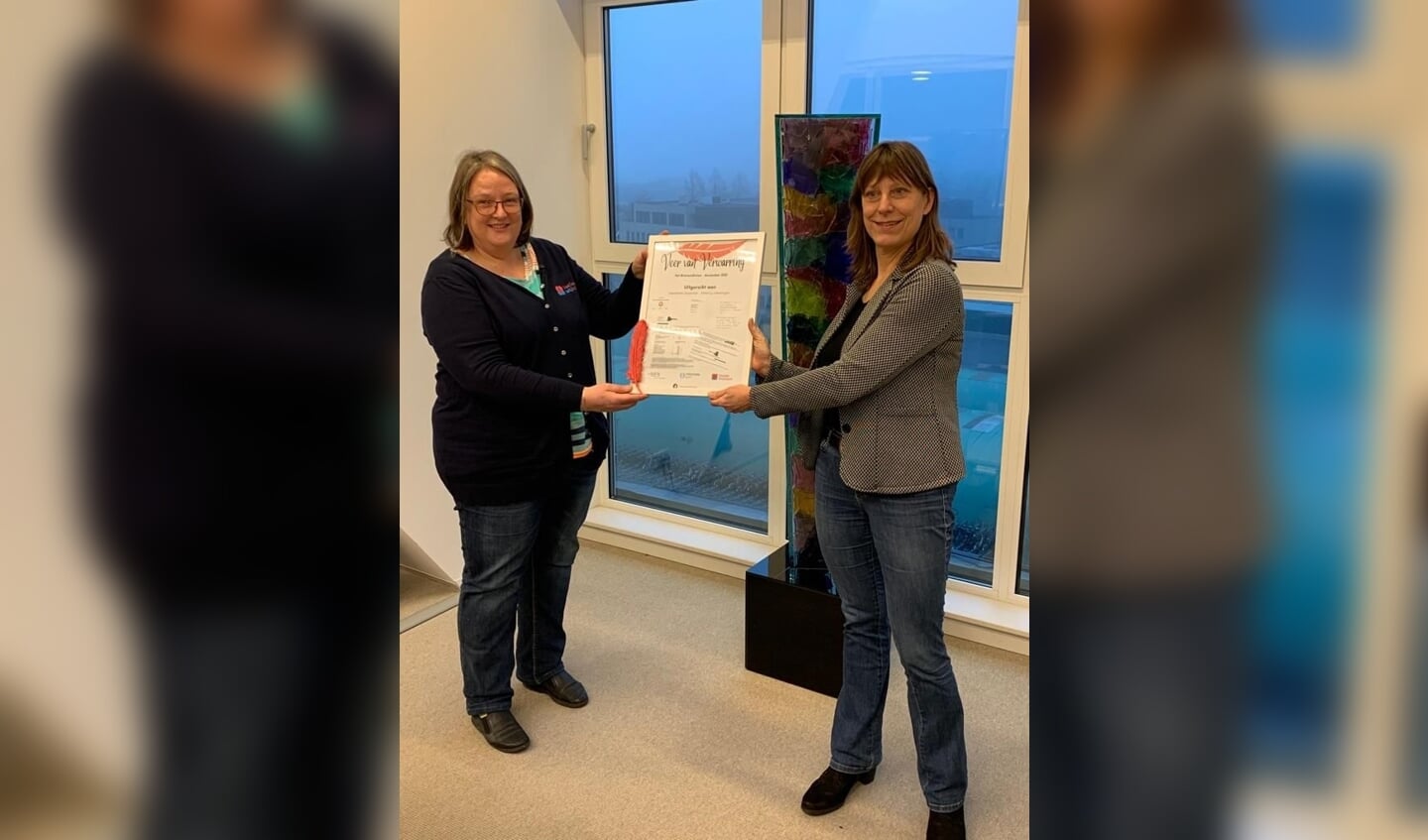 Wethouder Natasja Groothuismink nam de Veer van Verwarring in ontvangst uit handen van Mariëtte Klaren van het Sociaal Wijkteam Krommenie.