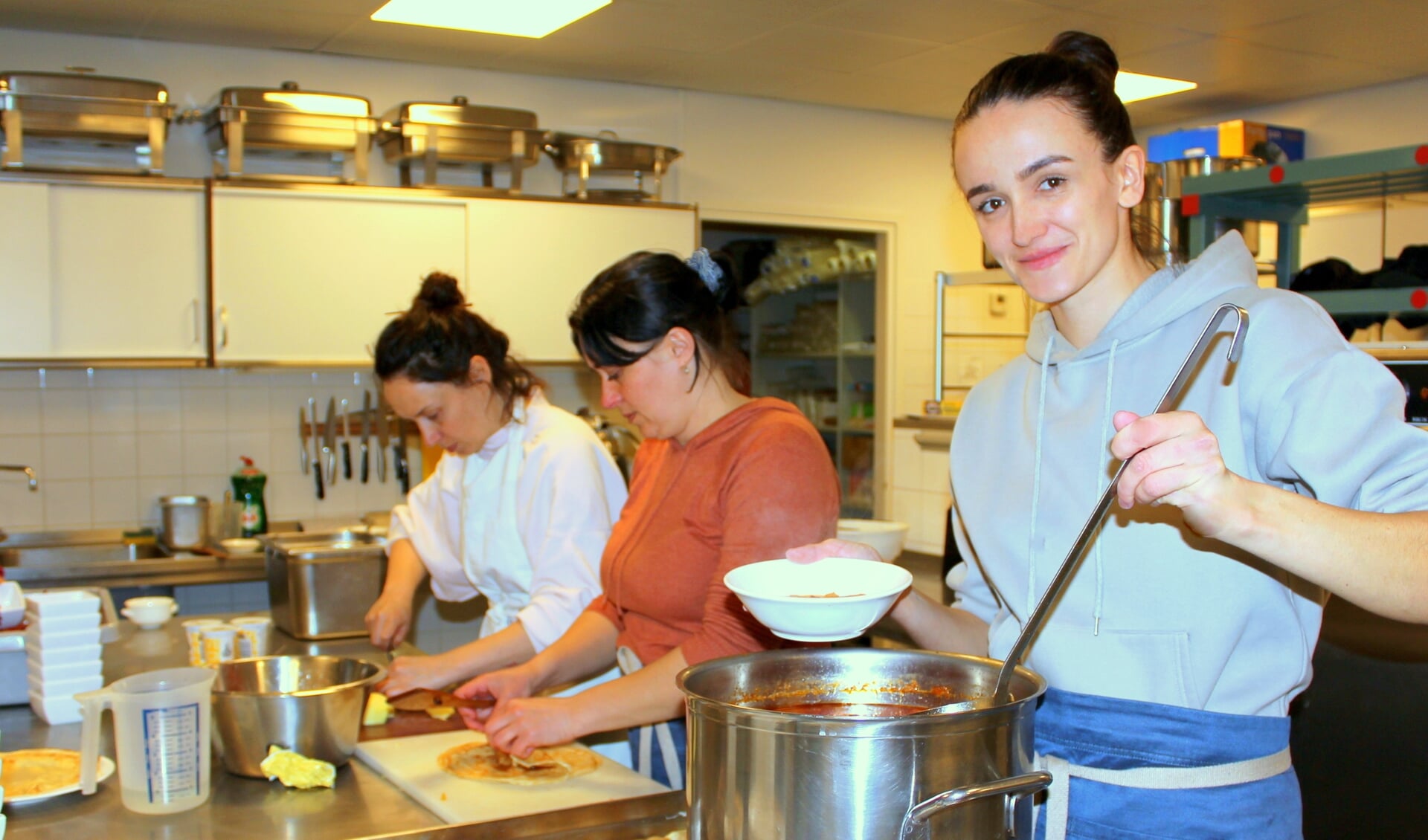 Alina (29) schept rode bietensoep in een kom. Net als Inna (li) en Yuliia (midden) is ze gevlucht uit Oekraïne. Samen met andere vluchtelingen doet het drietal mee aan een maaltijdproject in Hazerswoude-Dorp, waarbij ze koken voor de inwoners.