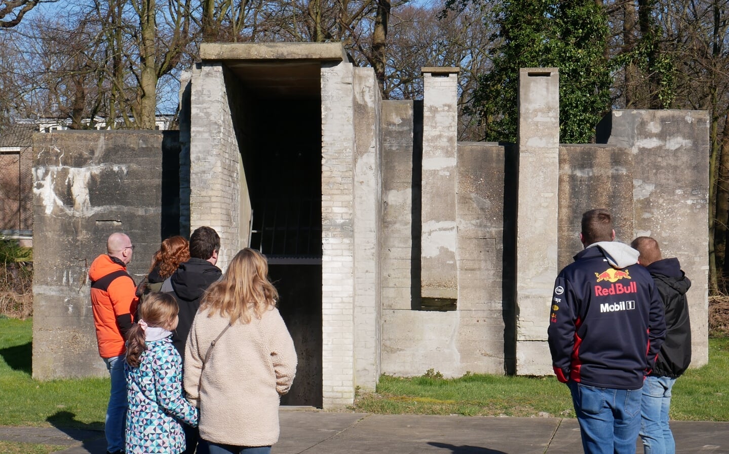 Jong en ouder publiek luistert aandachtig naar de rondleiding bij een van de bunkers op het terrein.