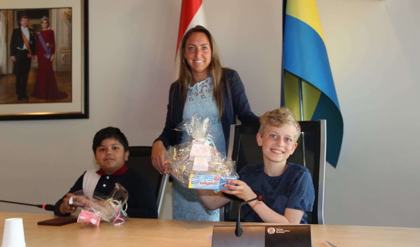 Jenish (l) en Jasper samen met wethouder Larissa Bentvelzen in de raadzaal op de plek van de burgemeester.