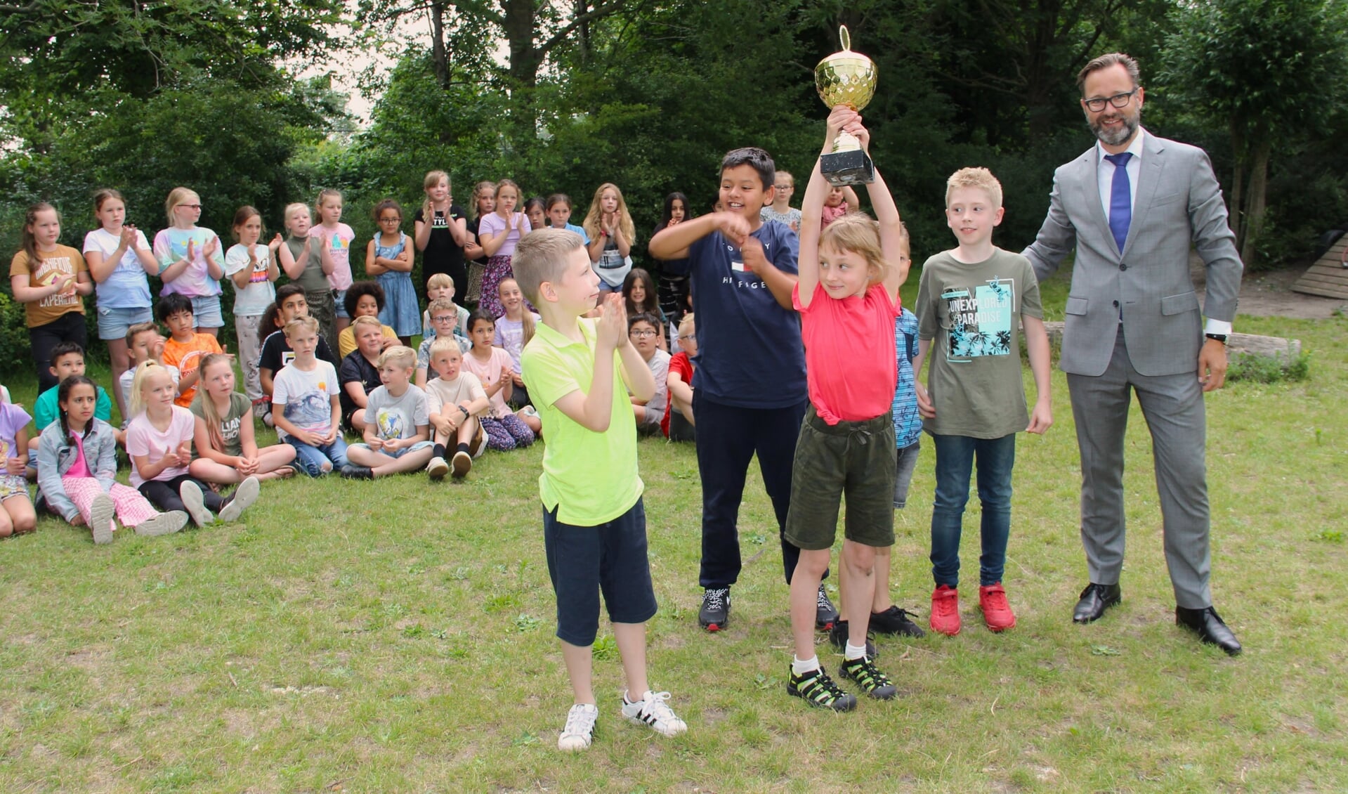 Een leerling van de winnende Wethouder Brederodeschool houdt trots de Helden van Rijswijk-wisseltrofee in de lucht. Rechts kersverse wethouder Milieu & duurzaamheid, Mark Wit.