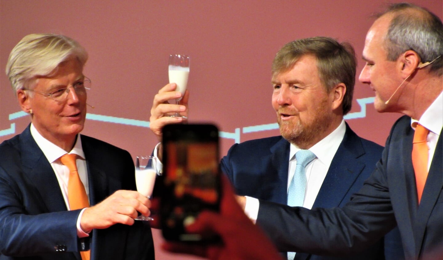 Koning Willem-Alexander heft samen met Alexander van der Lely, links van hem en Andre van Troost, rechts van hem, het melkglas op de zojuist door hem geopende vernieuwde Lelycampus.