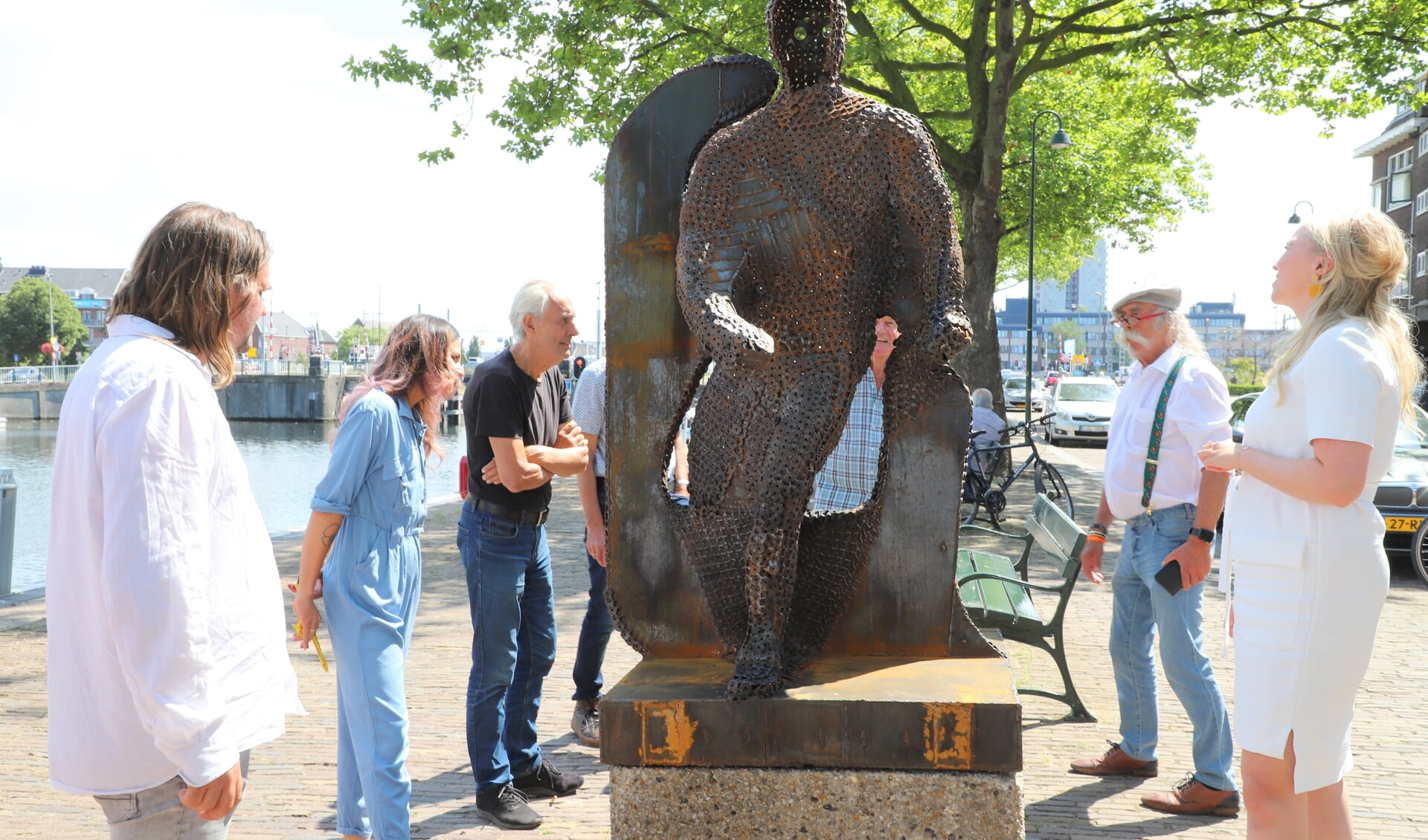 Belangstellende Vlaardingers, onder wie nachtburgemeester Leonardus IJdo, observeren het monument dat zojuist onthuld is door Frans de Winter en Lianne van Kalken, links en rechts op de foto.