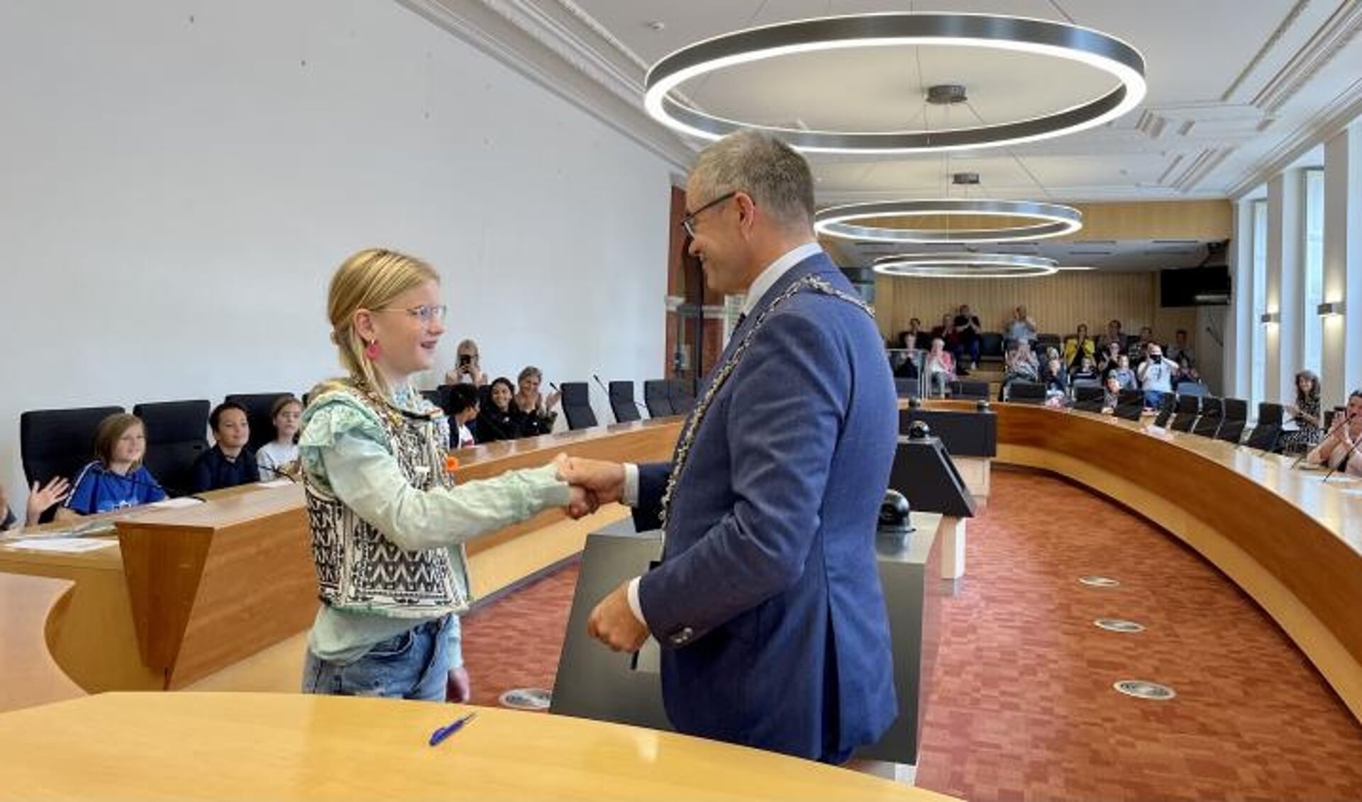 Kinderburgemeester Tess schudt de hand met burgemeester Jos Wienen tijdens de installatie van de nieuwe kinderraad. 