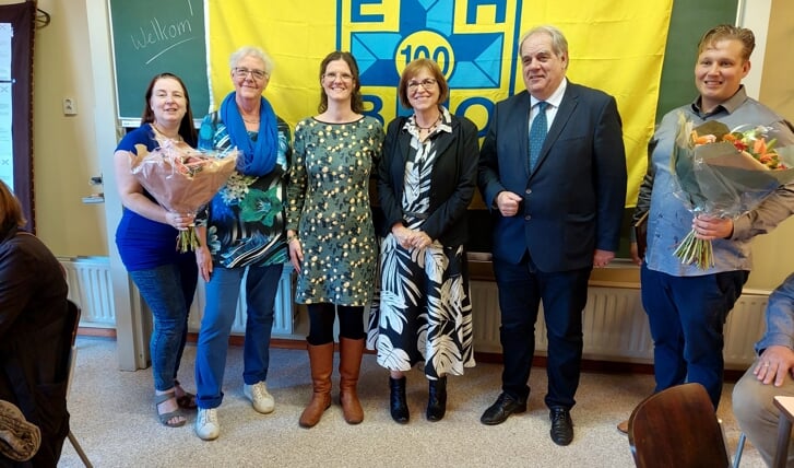 Het bestuur van de EHBO vereniging Rijswijk poseert met de speciale vlag voor het honderdjarig bestaan, die ze heeft ontvangen van de landelijke KNV EHBO. Burgemeester Bas Verkerk is aandachtig toeschouwer.