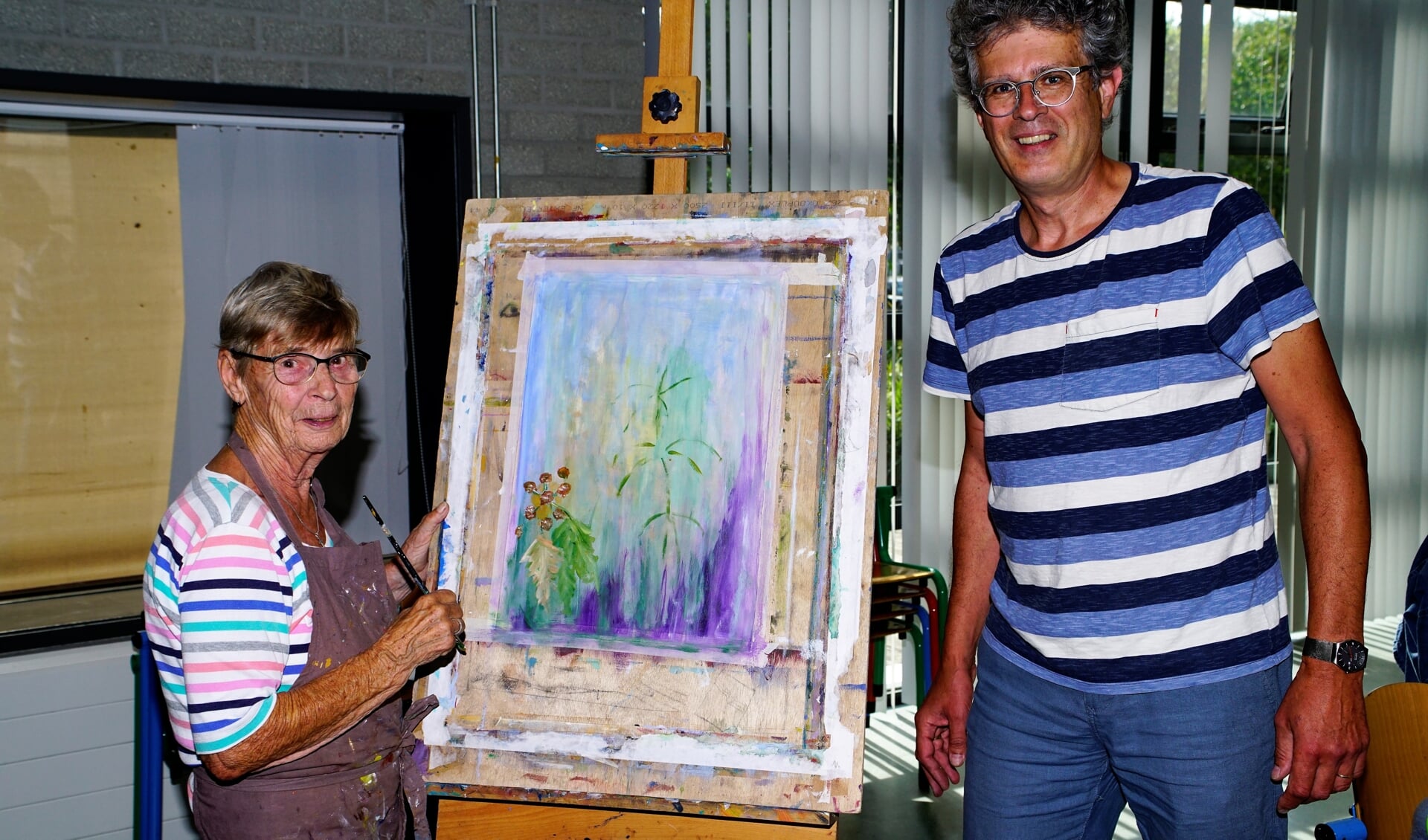 Ria de Groot en Hans Verbeek bij een schilderij van Ria. Naast schilderijen doen ook andere disciplines mee met de wedstrijd. 