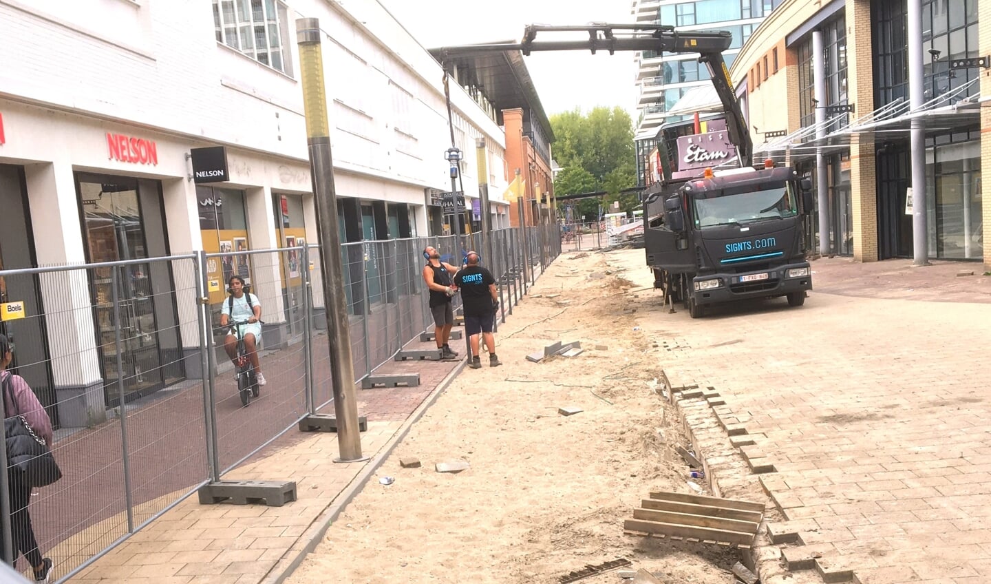Achter de hekken wordt de bestrating verwijderd. De mannen op de foto zijn begonnen de palen voor de permanente bouwschutting neer te zetten.