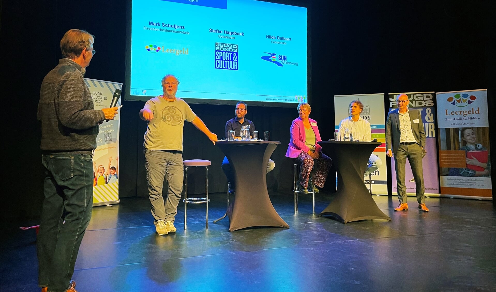 Van links naar rechts: Presentator Theo Werner, Hans Spekman (directeur Jeugdeducatiefonds), Mark Schutjens (directeur-bestuurssecretaris Stichting Leergeld),Hilda Dullaart (coördinator SUN Waterweg), Stefan Hagebeek (coördinator Jeugdfonds Sport & Cultuur) en John Massaar (directeur Fonds Schiedam Vlaardingen e.o.).