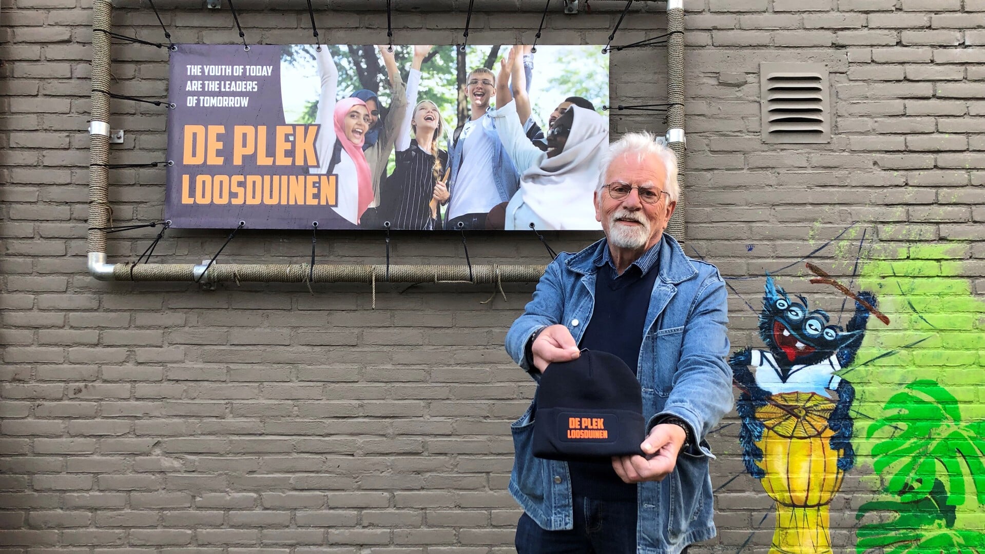 Jan Janssen toont trots één van de petten die zijn gemaakte voor de opening van De Plek.
