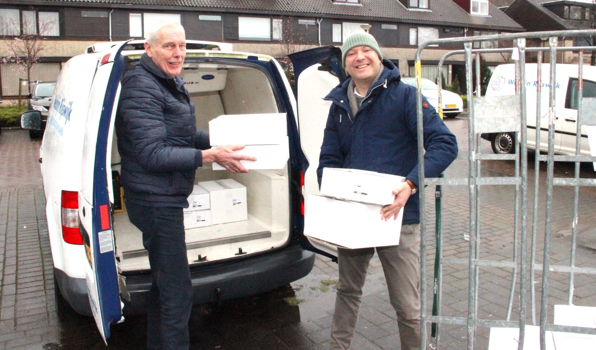 Vrijwilligers Hans (l.) en zijn bijrijder wethouder Armand van de Laar laden de maaltijden in de stromende regen in de koelwagen van Welzijn Rijswijk.